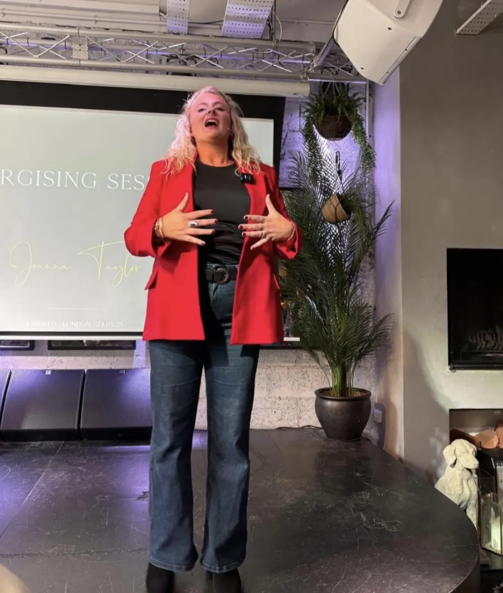 Jo Taylor presenting an energising session on stage in a red blazer